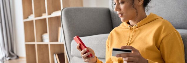 A woman holding her phone in one hand and her credit card in the other.